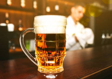 Ahşap tezgahın üzerinde köpüklü bir bardak bira duruyor. Barmenin arka planda bulaşıkları yıkadığı eski bir bar. Boş zaman, eğlence ve arkadaşlar fotoğraf kavramları.