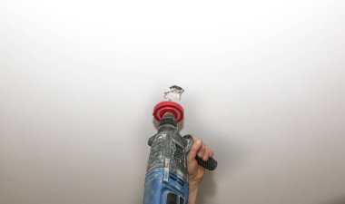 Lamba kurulumu. Tavanda elektrikli matkapla delik açan bir adam. Kapalı alanda restorasyon. Bakım işi.