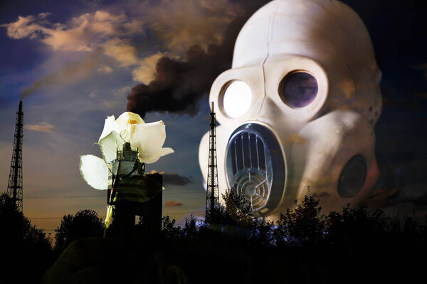Man in the gas mask holding yellow luminous flower. Radiation influence. Environmental pollution. Chernobyl concept. Dangerous nuclear power. Ecological disaster. Factory pipe with smoke.