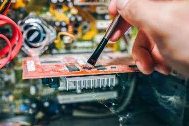 Eski kişisel bilgisayarın içinde. Anakart ve video kartı toz içinde. Adam telleri fırçayla temizliyor. Kırık PC.