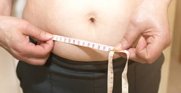 Overweight man measuring waist with measure tape, close up image. Weight  loss, motivation, fat burning Stock Photo