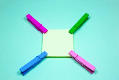 Renkli ahşap mandallı boş sarı çıkartma. Mavi arkaplandaki not kağıdını kapat. Boşluğu kopyala.