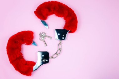 Pembe arka planda anahtarları olan kırmızı seksi tüylü kelepçeler..