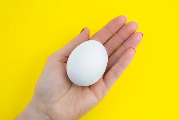 White egg in woman hand on the yellow background. Copy space. Minimalism, original and creative photo. Beautiful wallpaper. Easter holidays.