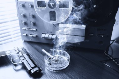 Dinleme için teyp kaydı. KGB casusluk konuşmaları. Siyah silah yakında. Sigaralı kül tablası.