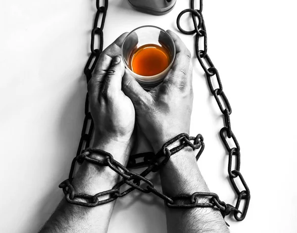 Man\'s hands in old rusty chains near the bottle. Addicted to alcohol. Dangerous habit.