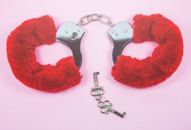 Pembe arka planda anahtarları olan kırmızı seksi tüylü kelepçeler..