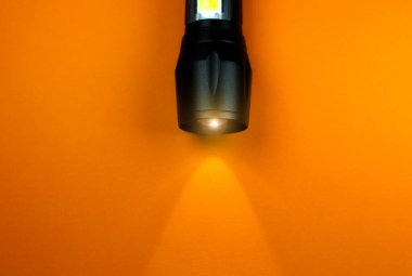 Siyah el feneri ve turuncu arka planda bir ışık demeti. Fotoğrafı kapat..