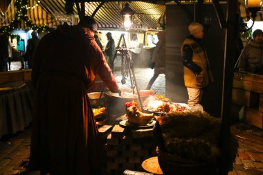 RIGA, LATVIA - 5 Aralık 2018: Noel zamanı Riga şehir merkezi. Turistik gezi konsepti. Sosis ve domuz kızartması yapan adam. Izgara sokak yemeği..