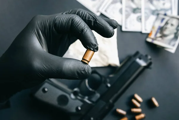 Gun lying on the table. Man in black gloves holding bullets. Illegal drug selling. Criminal problems. Dollars.