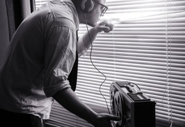 Özel ajan bobin kayıt cihazını dinliyor. Memur kulaklıkla dinleme yapıyor. Pencereden gözetlemek. Eski panjurlar. siyah ve beyaz.