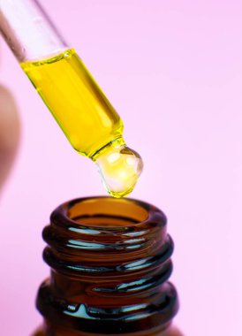 Pembe arka planda pipetli bir şişe kozmetik yağı. Damlayan sıvıyı kapat. Güzellik, ilaç ve sağlık hizmetleri konsepti. Makro fotoğraf. Doğal, eko kozmetik.