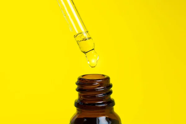 Bottle of cosmetic oil with a pipette on a yellow background. Close up liquid drop dripping. Beauty, medicine and  health care concept. Macro photo. Natural, eco cosmetics.
