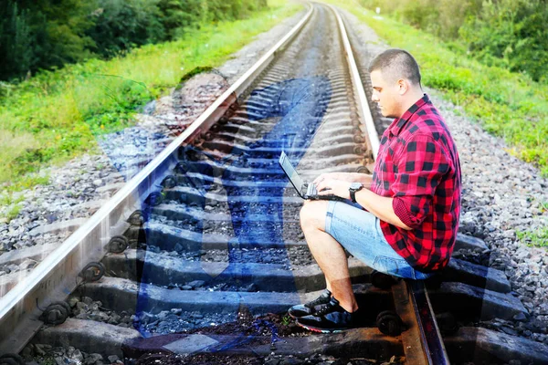 Ofis serbest çalışma kavramına karşı. Dizüstü bilgisayarı olan adam rayların üzerinde oturuyor. Yorgun bir ofis çalışanının resmi. Seyahat sırasında çalışma.