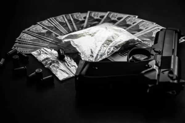 Gun with bullets lying on the table. Criminal problems. Drugs and money on black background. Illegal selling. Black and white photo.