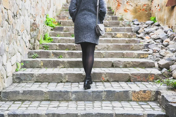 stock image Girl is walking in the narrow street with stone pavement. Stylish woman with a leather bag. Stairs in the city.