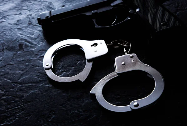 Siyah çelik tabanca ve polis metali gerçek kelepçeler siyah arka planda yatıyor. Özel dedektiflik işi. Bilgi aranıyor. Suç ve soygun, hapishane kavramı.