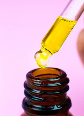 Pembe arka planda pipetli bir şişe kozmetik yağı. Damlayan sıvıyı kapat. Güzellik, ilaç ve sağlık hizmetleri konsepti. Makro fotoğraf. Doğal, eko kozmetik.
