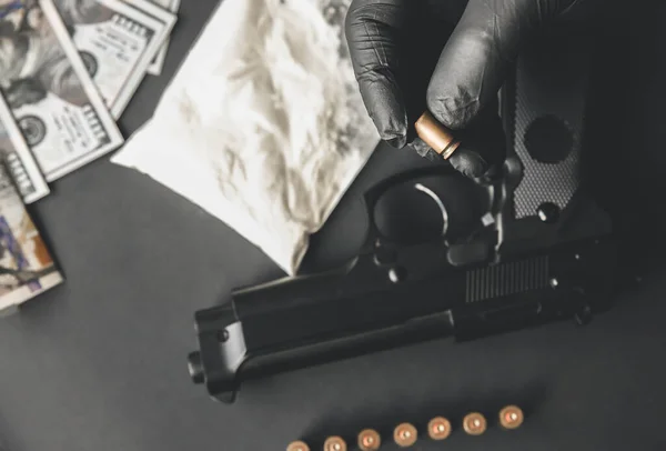 Gun lying on the table. Man in black gloves holding bullets. Illegal drug selling. Criminal problems. Dollars.