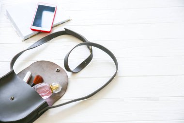 Telefon, şık çanta ve beyaz arka planda parfümler. Güzel düz bir yatak. İş kadını için eşyalar. Not defteri çizelgesi. Makyaj seti.