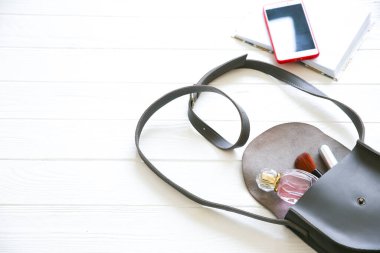 Telefon, şık çanta ve beyaz arka planda parfümler. Güzel düz bir yatak. İş kadını için eşyalar. Not defteri çizelgesi. Makyaj seti.