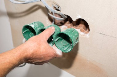 İnsanlar elektrik üretiyor. Bakım onarımı dairede tadilat yapıyor. Kapalı alanda restorasyon. Duvardaki deliklerde soket anahtarları için renkli kablolar var..