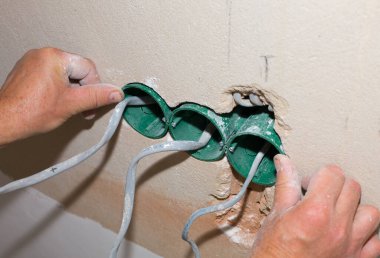 İnsanlar elektrik üretiyor. Bakım onarımı dairede tadilat yapıyor. Kapalı alanda restorasyon. Duvardaki deliklerde soket anahtarları için renkli kablolar var..