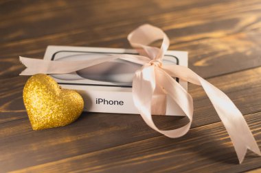 KYIV, UKRAINE - 05 Ocak 2026: Modern akıllı telefon Apple iPhone, altın kalp oyuncağının yanında pembe kurdeleyle sarılmış bir hediye gibi. Romantik bir hediye ver..