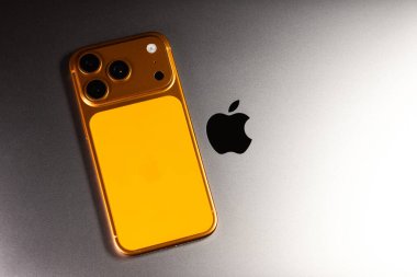 KYIV, UKRAINE - 22 Ocak 2026: Apple iPhone 17 Pro in cosmic Orange color is lie on gray Macbook Pro laptop. Apple şirketinin logosu, kapat..