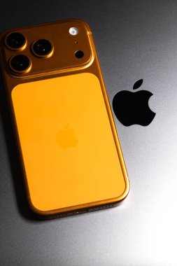 KYIV, UKRAINE - 22 Ocak 2026: Apple iPhone 17 Pro in cosmic Orange color is lie on gray Macbook Pro laptop. Apple şirketinin logosu, kapat. Dikey fotoğraf.