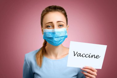 Tıbbi maske takan genç bir kız koronavirüs aşısını bekliyor. Bir kadın elinde yazıyla bir tabela tutuyor. İlacın geliştirilmesini bekliyor. Covid19 saniye dalgası