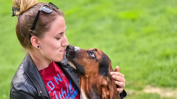 Young woman with an affectionate one year old Basset hound (Canis lupus familiaris) in the yard of a hobby farm. — Stock Photo, Image