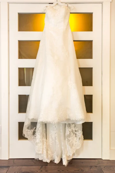 Wedding dress hanging on a door in warm bedroom light. — Stock Photo, Image