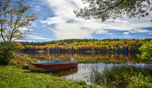 Ein Fischerboot an einer Anlegestelle und Herbstfarbe leuchtet Ende September auf einem See und Wald. — Stockfoto