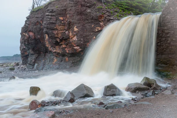 Printemps Côte de la Nouvelle-Écosse en juin. Cascades d'une falaise sur une plage de galets rocheux . — Photo