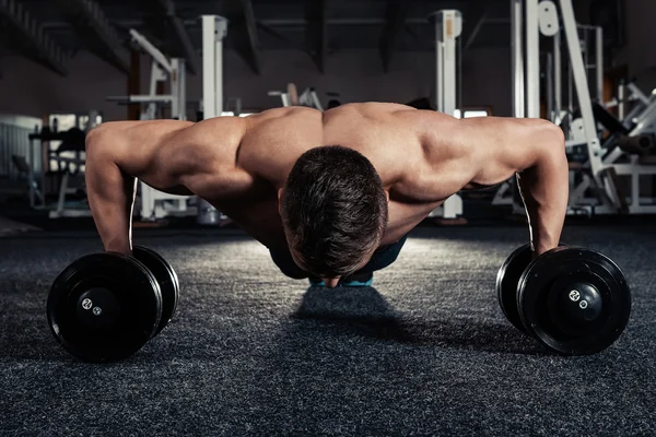 Bonito homem musculoso fazendo exercícios de flexões com halteres — Fotografia de Stock