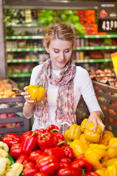 Retrato de una hermosa mujer joven eligiendo verduras en la tienda de comestibles — Foto de Stock