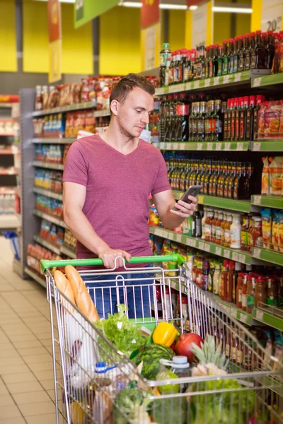 Hombre joven usando el teléfono móvil en el supermercado — Foto de Stock