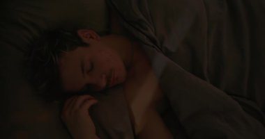 Genç adam karanlık bir yatak odasında uyanıyor.