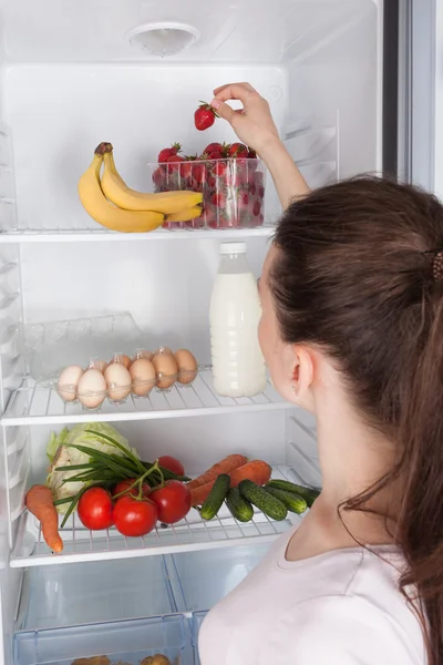 Young cheerful woman taking a strawberry  from refrigerator — Stock Photo, Image