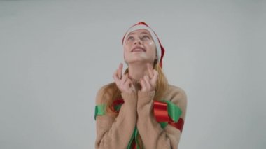 Noel Baba şapkalı bir kız dua ediyor. Gümüş bir arka planda Noel arzuları.