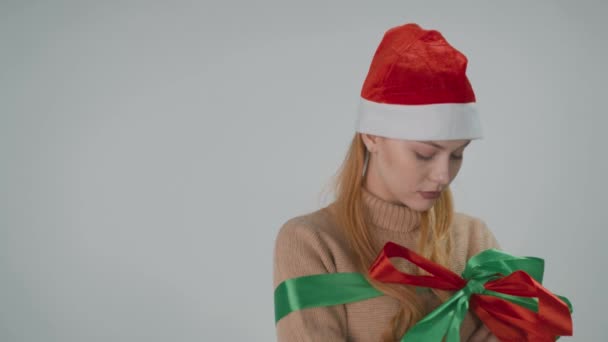 Молода дівчина в капелюсі Миколая посміхається на Новий Рік подарунок, який вона отримала.. — стокове відео