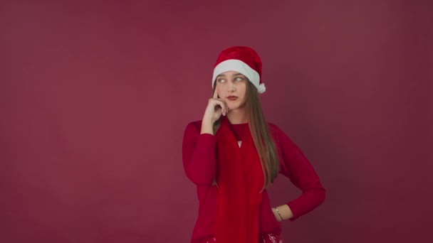 Sladký pohled a jemný úsměv. Dívka v santa klobouk pózovat na červeném pozadí. — Stock video