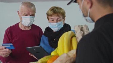 Kurye teslimatıyla alışveriş yapan ve kredi kartıyla ödeme yapan yaşlı bir aile. Online konsept ve salgın konsepti