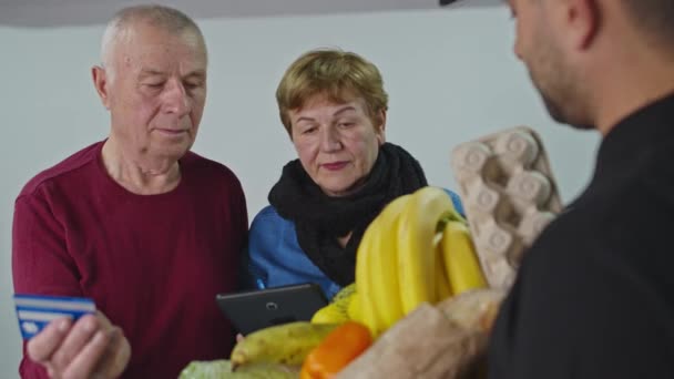 Een bejaarde familie betaalt per creditcard voor koeriersbezorging. Senior online concept en pandemisch concept — Stockvideo