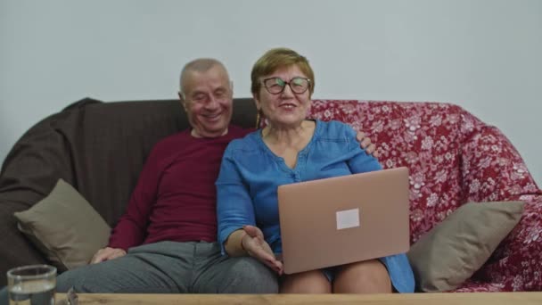 Een oudere vrouw gebruikt een laptop en lacht gelukkig. De man zit naast hem en houdt het gesprek gaande.. — Stockvideo