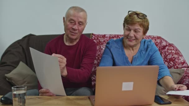 De oudere echtgenoot betaalt via het internet vanaf een laptop. Pandemisch concept — Stockvideo