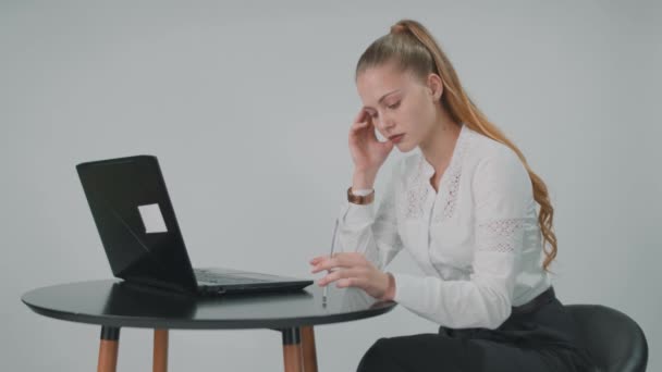 Jovem mulher pensativa está sentado perto do computador segurando uma caneta em seu braço. — Vídeo de Stock