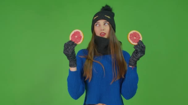 Una chica está vestida con un jersey azul y una bufanda roja sosteniendo rodajas de pomelo.. — Vídeos de Stock