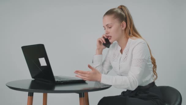 Vrouw beantwoordt de telefoon zittend bij de computer in kantoorkleding. — Stockvideo